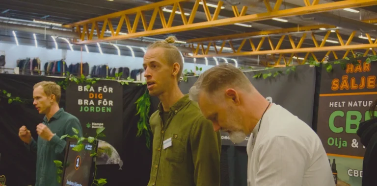 Två män från Hampablomman pratar med en besökare i montern på Harmoni Expo, med skylten “Bra för dig, bra för jorden