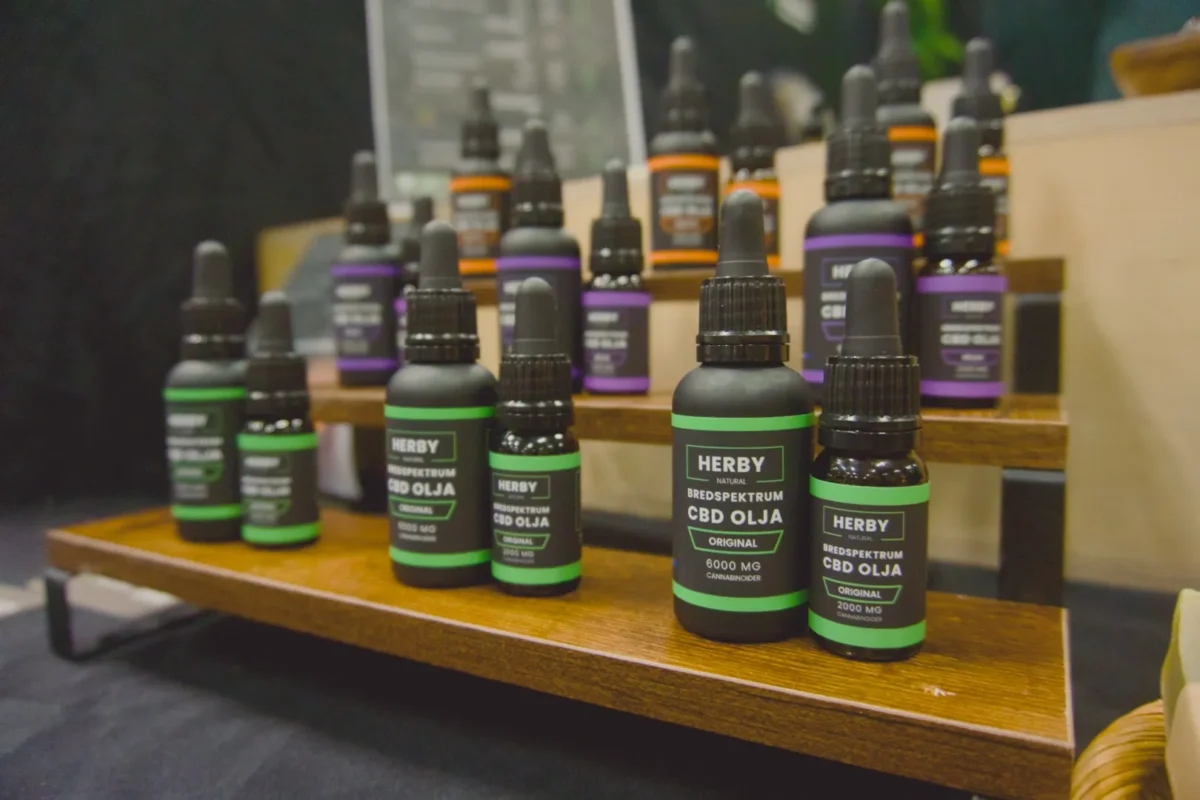 Herby bredspektrum CBD-olja Original i 2000 mg och 6000 mg på en trähylla, med lila och orangea varianter bakom