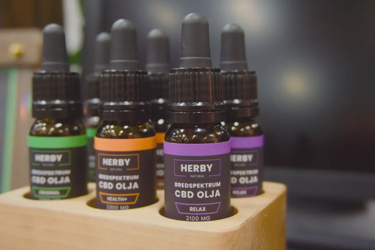 Tre Herby bredspektrum CBD-oljor i träställ: Original (grön), Health+ 2300 mg (orange) och Relax 2100 mg (lila)