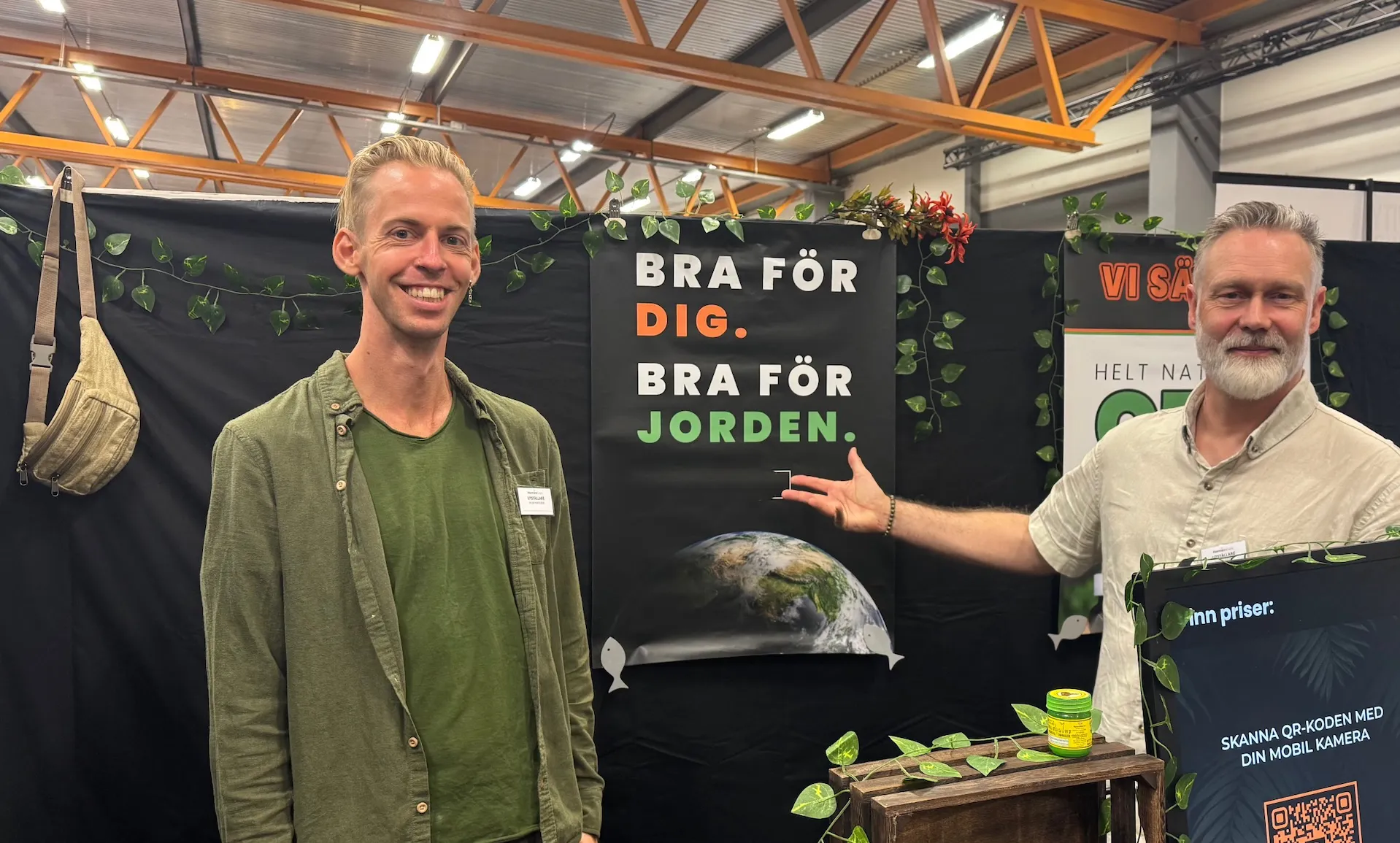Två utställare i Hampablommans nya monter på Harmoni Expo våren 2025, med affisch och skylt med QR-kod för priser