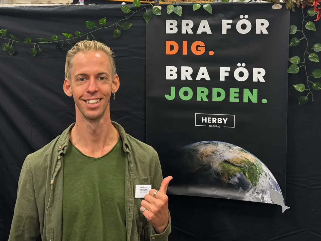 Man med tummen upp framför affischen “Bra för dig. Bra för jorden.” i Hampablommans monter på Harmoni Expo våren 2025